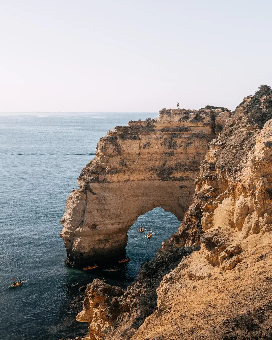 Limestone cliff in the ocean with canoes around it.